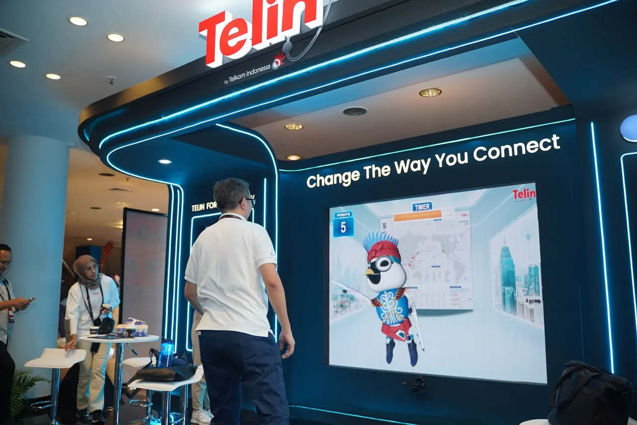 Visitor playing an interactive game on the Telin booth wall, framed by neon blue light strips